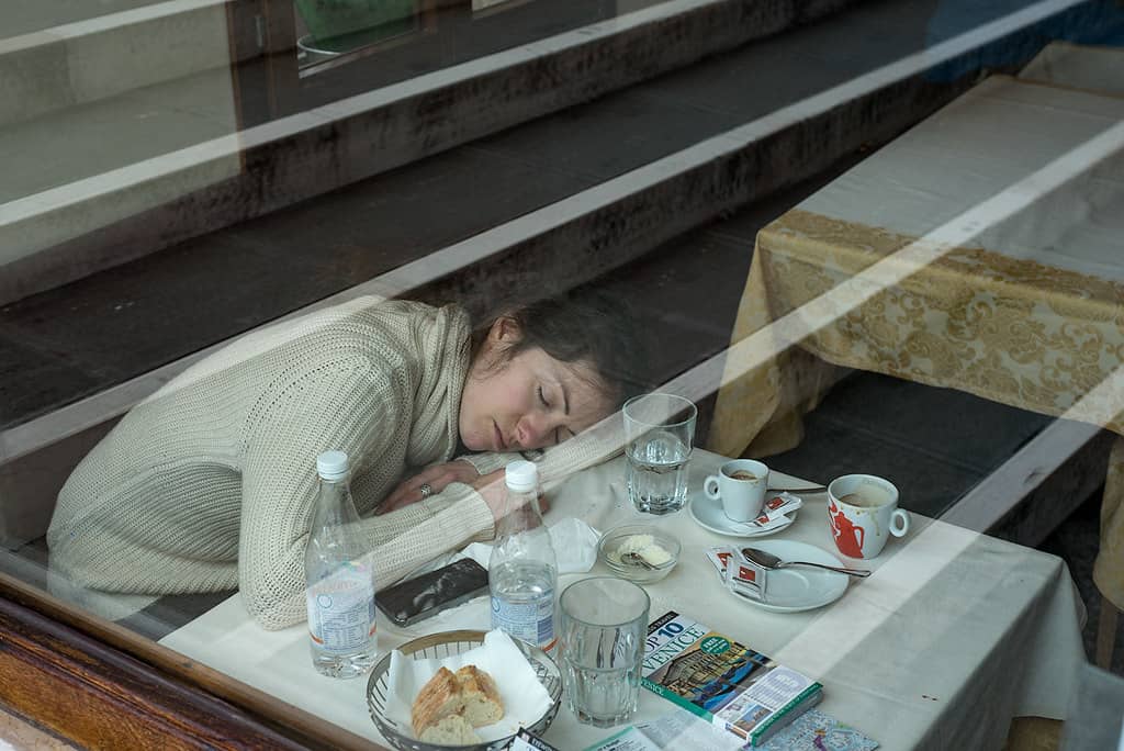 A woman peacefully sleeping at a table in a restaurant, seemingly unaware of the bustling atmosphere around her.