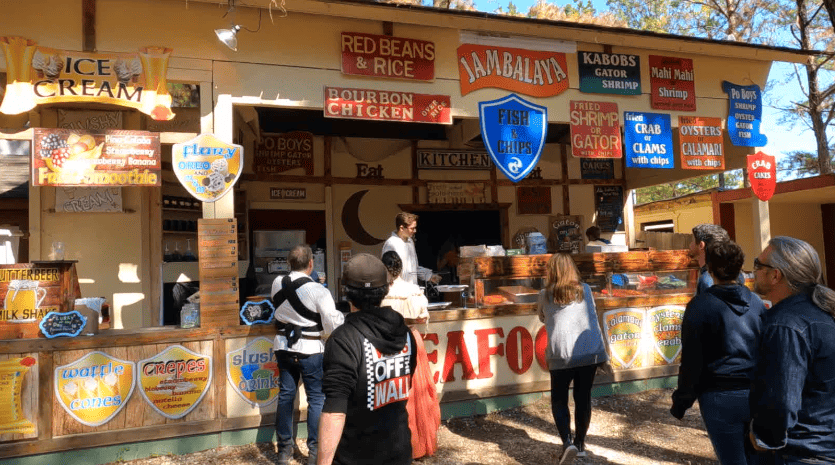 Food booth selling turkey legs, roasted vegetables, Jambalaya, seafood, and more.